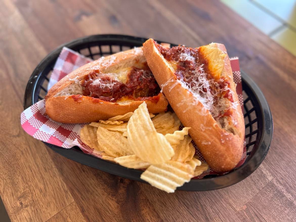 Nonna's meatball sub with parmesan and chips in a red check basket