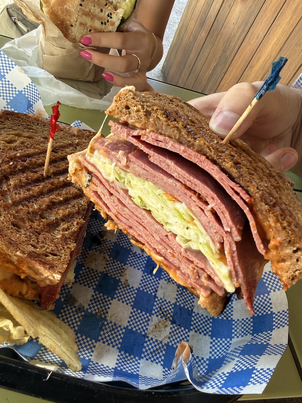 A pastrami panini on rye in a blue check basket