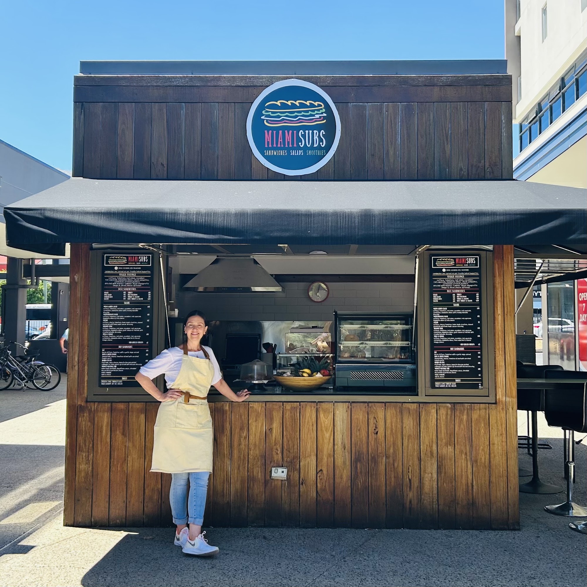 The Miami Subs timber kiosk with its black awning, menu boards and the owner at the window